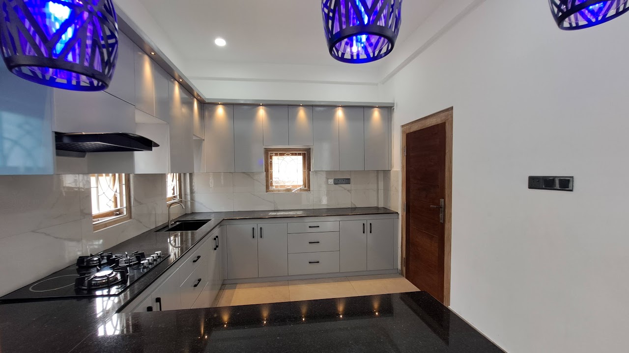 Light grey fitted kitchen cabinets with black counters and lighting above the upper cabinets