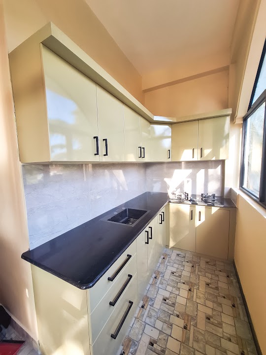 Gloss cream L-shaped fitted pantry cabinetry with black countertops and modern hardware