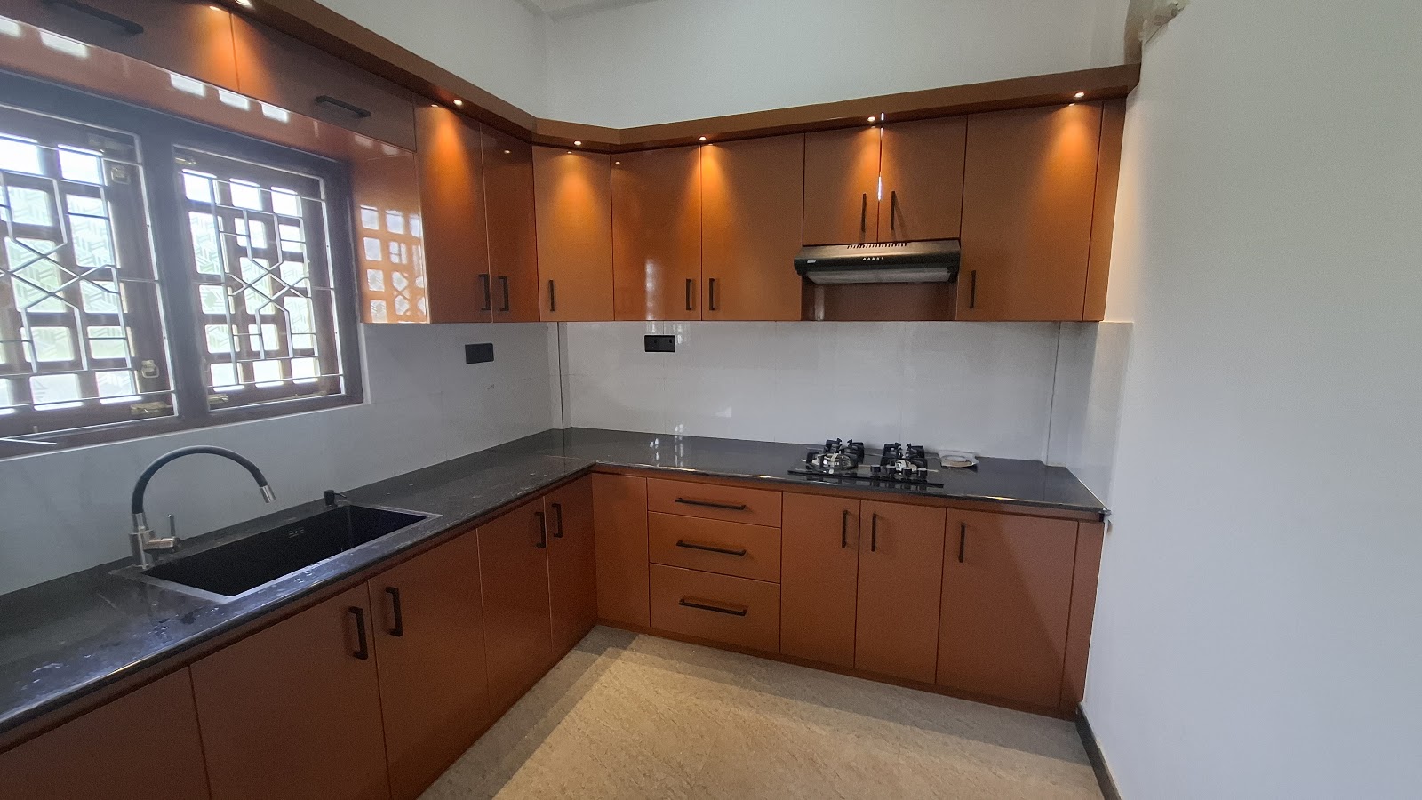 Warm timber-toned L-shaped kitchen with dark worktops and illuminated wall cabinets